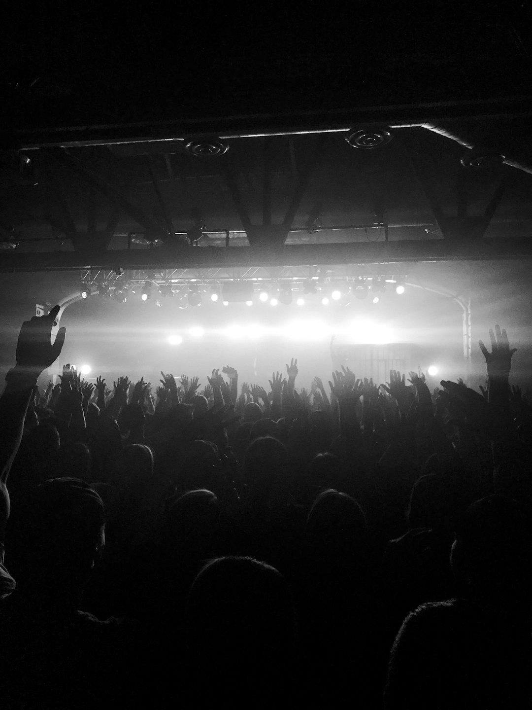 Hände bei einem Indoor-Konzert mit hellen Bühnenlichtern erhoben.